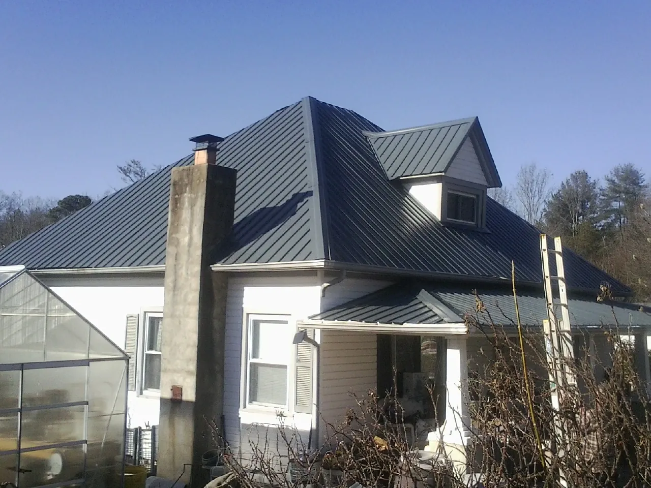 Dark blue standing seam metal roof on a white farmhouse with dormer — Slate & Tile Roof Repair by Roofing Brothers in Montgomery Village