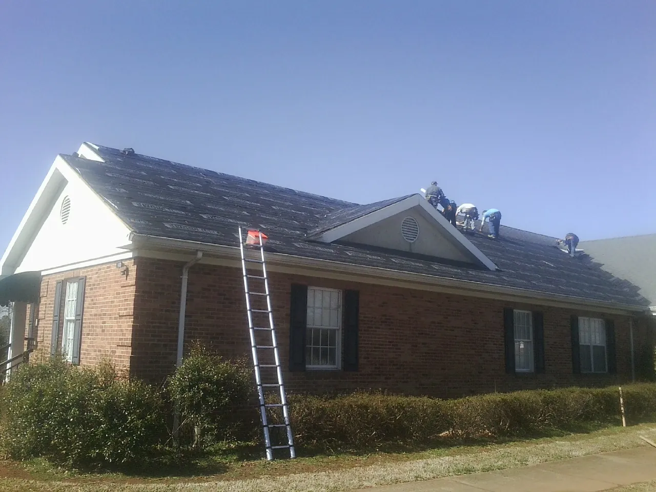 Crew tearing shingles off a brick ranch roof with a ladder set — Metal Roof Repair work by our crew in Montgomery Village