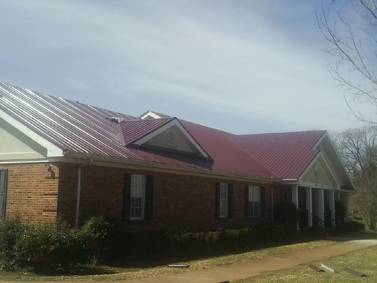 Red metal roof with gabled entries on a long brick building, from a Hail Damage Roof Repair job in Montgomery Village
