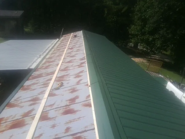 Old rusted panels beside newly installed green metal roofing — Wind Damage Roof Repair by Roofing Brothers in Montgomery Village