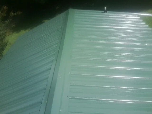 New green metal panels meeting at the ridge of a roof — Flat Roof Repair work by our crew in Montgomery Village