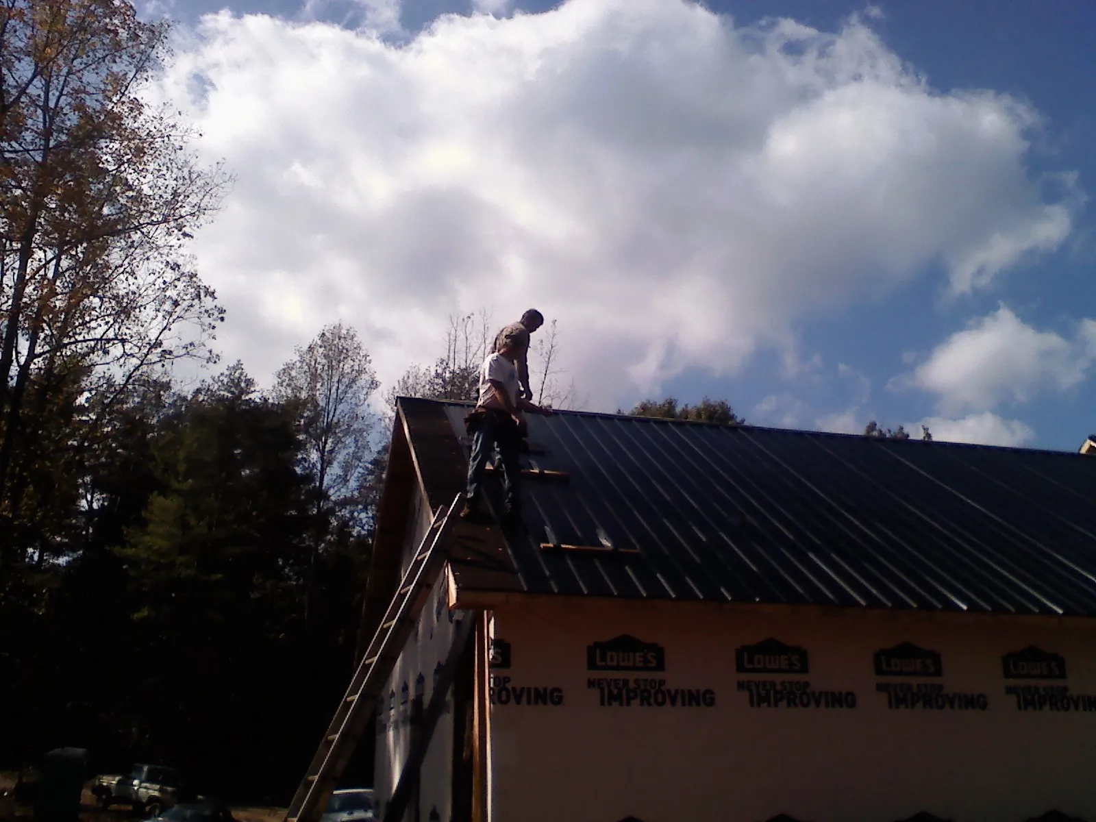 Roofer fastening dark metal panels high against a cloudy sky, from a Roof Inspection job in Montgomery Village