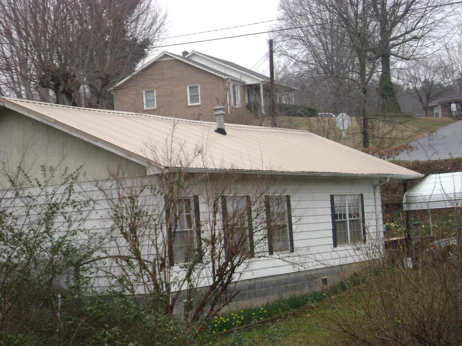 Tan metal roof on a white sided house set into a hillside — Commercial Roofing by Roofing Brothers in Montgomery Village